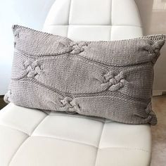 a white leather chair with a gray knitted pillow sitting on it's back