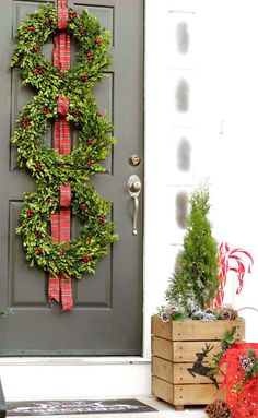 a christmas wreath is hanging on the front door with red and green ribbons around it