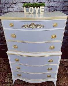 a white and gold dresser with love written on it's top, in front of a brick wall