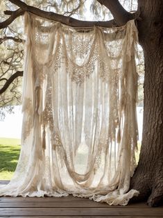 an open window with sheer curtains hanging from it's sides next to a tree