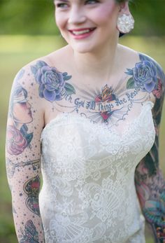 a woman in a wedding dress with tattoos on her arms and shoulder smiling at the camera