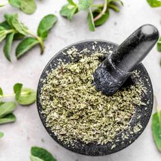 a blender filled with herbs on top of a white table next to green leaves