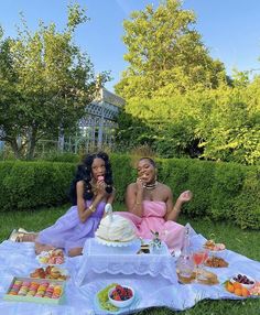 two women sitting on the grass eating cake