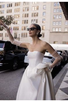 a woman in a white dress and gloves on the street with her arm outstretched up