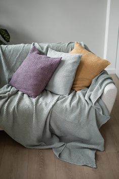 a couch covered in blankets and pillows on top of a wooden floor next to a potted plant