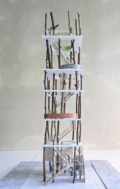 a sculpture made out of sticks and paper on top of a cement floor with a wall in the background