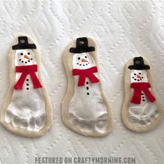 three snowmen made out of cookies sitting on top of a white sheet with red ribbon