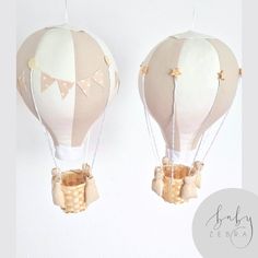 two hot air balloons with bows hanging from strings on the ceiling, one is white and the other is beige