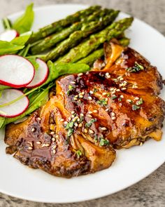 a plate with meat, asparagus and radishes on it next to a glass of water