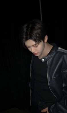 a young man in a black jacket looking down at his cell phone while standing up