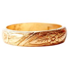 a gold wedding band with flowers and leaves on the inside, in front of a white background