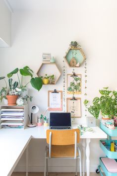 a white desk topped with a laptop computer next to a plant filled wall behind it