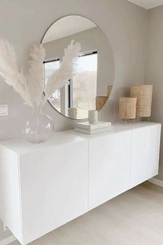 a white dresser topped with a mirror and vase filled with feathers