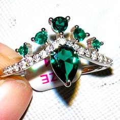 someone is holding a ring with green and white stones