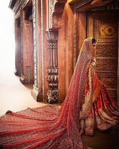 a woman in a red and gold bridal gown standing next to an ornate wooden door