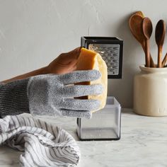 a person wearing gloves and holding a loaf of bread in front of a toaster