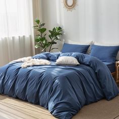 a bed with blue comforter and pillows in a room next to a plant on the floor