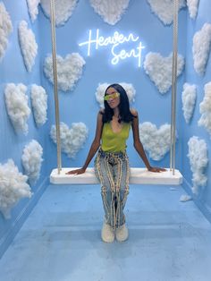 a woman standing in front of a blue wall with clouds on it and the words heaven song above her head