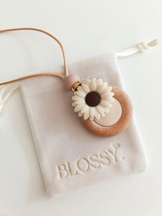 a necklace with a flower on it sitting on top of a white cloth bag that says blossom