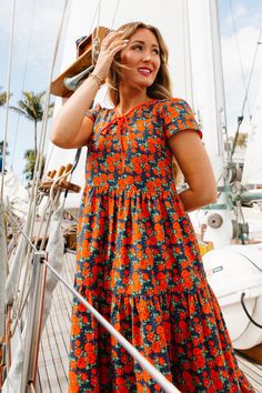 Step into summer with our brand new Kenna Dress! She's a vibrant dress adorned with a cheerful floral pattern. This charming dress features a darling bow detail at the neckline along with a tiered skirt and short sleeves! This lightweight fabric creates a breezy, simple silhouette, perfect for warm, sunny days. Ideal for any adventure, the Kenna Dress is your go-to for effortlessly chic & joyful summer days. Floral Print A-line Sundress, Yellow Ditsy Floral Print Sundress, Yellow Floral V-neck Sundress, Yellow V-neck Sundress With Floral Print, Yellow Floral Print V-neck Sundress, Vibrant Dress, City Woman, Simple Silhouette, Cotton Maxi