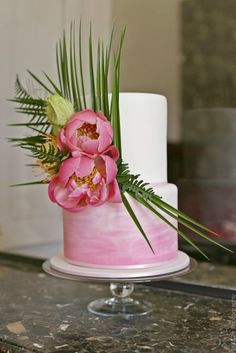 a pink wedding cake decorated with flowers and palm fronds is displayed on the instagram page