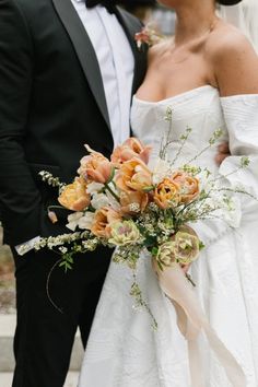 the bride and groom are kissing each other in their wedding day attire, with one holding a bouquet of flowers