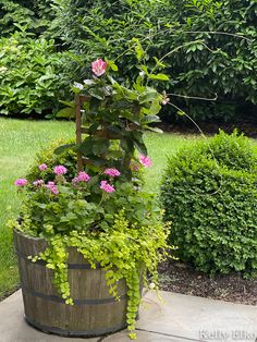 a wooden barrel filled with lots of flowers and greenery next to some shrubbery