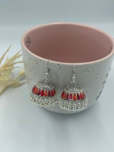 These silver jhumka earrings are a perfect expression of your unique style and personality. They exude a fiery charm and exuberance, making them a perfect choice for those who love bold and vibrant jewelry. Wear them to make a statement, stand out from the crowd, and add a touch of elegance and flair to any outfit. Indulge in the allure of silver jhumka earrings with red and orange hues, available exclusively in our collection. Order now and adorn yourself with the beauty and vibrancy of these exquisite earrings that are sure to become a cherished addition to your jewelry collection! These jhumka earrings are lightweight and comfortable to wear, making them ideal for special occasions, festivals, or everyday wear. They are crafted with high-quality materials to ensure durability and longev Multicolor Earrings For Navratri Puja, Multicolor Earrings For Diwali Puja, Multicolor Latkans Earrings For Puja, Multicolor Earrings For Puja, Fusion Style Jhumkas For Navratri Gift, Multicolor Latkan Earrings For Puja, Red Fusion Style Chandbalis For Diwali, Red Fusion Drop Earrings, Red Fusion Style Drop Earrings