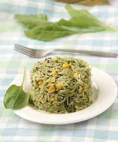 a white plate topped with green rice next to a fork and leafy greens on a checkered table cloth