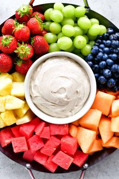 a platter filled with fruit and dip surrounded by grapes, strawberries, melon, kiwis, watermelon, blueberries