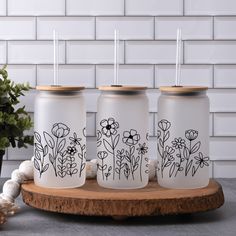 three painted mason jars sitting on top of a wooden board next to a planter