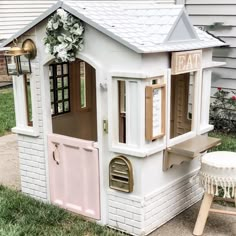 a white doll house sitting on top of a grass covered lawn next to a chair