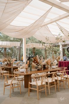 an outdoor dining area with tables and chairs covered in white tarps, surrounded by greenery