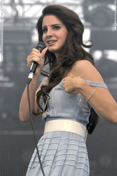 a woman holding a microphone in her right hand and wearing a dress on the other side