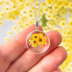 A beautiful sunflower themed pendant encased in a sterling silver round frame. The pendant is the perfect way to send someone special a bunch of bright, beautiful sunflowers. The sunflower pendant features a tiny, bunch of sunflowers, design surrounded by real pressed Queen Anne's Lace flowers preserved in resin.  Please note that the sunflowers themselves are not real pressed flowers. The pendant measures approximately 20mm in width and height excluding the bail.  The pendant is further decorat Sunflower Design Flower Jewelry For Anniversary, Sunflower Design Jewelry For Anniversary, Yellow Round Sunflower Jewelry, Yellow Sunflower Print Jewelry Gift, Yellow Sunflower Print Jewelry For Gift, Yellow Sunflower Print Jewelry As Gift, Sunflower Design Floral Jewelry, Dainty Sunflower Jewelry As A Gift, Sunflower Jewelry For Anniversary And Mother's Day