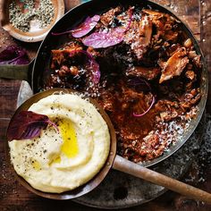 a pan filled with meat and mashed potatoes on top of a wooden table next to other dishes