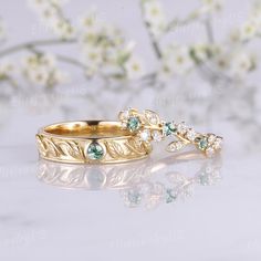 two gold wedding rings with green and white stones on them, sitting next to each other