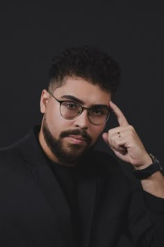 a man with glasses is posing for the camera while holding his hand up to his face