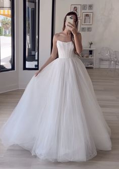 a woman taking a selfie wearing a white wedding dress in front of a mirror