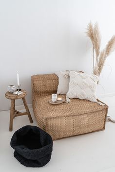 a wicker couch with pillows and a hat on the floor next to a small table