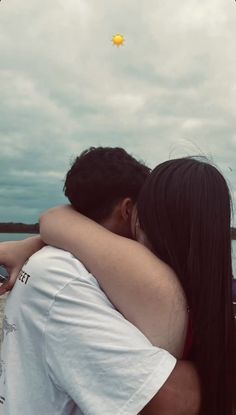 a man and woman hugging each other in front of the ocean with a kite flying above them