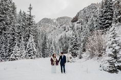 a bride and groom kissing in the snow surrounded by pine trees on their wedding day