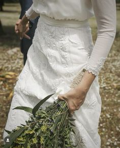 a woman in a white dress holding a bunch of greenery on her left hand