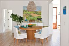 a dining room table with white chairs and a painting on the wall