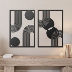 two black and white art pieces on a wall above a wooden table with a lamp