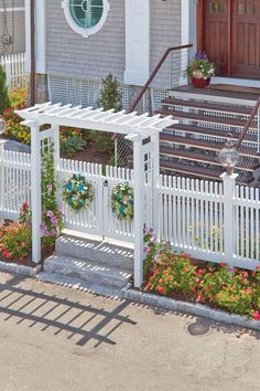 a white picket fence in front of a house with flowers on the ground and steps leading up to it