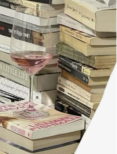 a glass of wine sitting on top of a pile of books next to each other