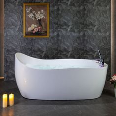 a large white bath tub sitting next to two vases with flowers in it and candles on the floor