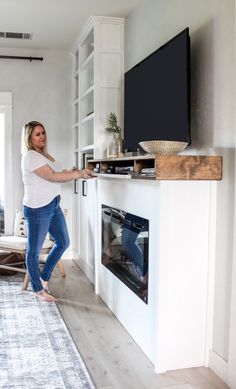 a woman standing in front of a flat screen tv on top of a white fireplace