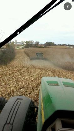 a tractor driving down a dirt road next to a field filled with grass and corn